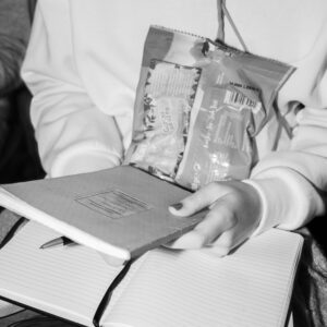 Eine Person hält zwei Notizbücher und Gummibärchen auf dem Schoß. Eines ist offen, eines geschlossen. Die Situation zeigt eine Auszubildende während eines Seminars.