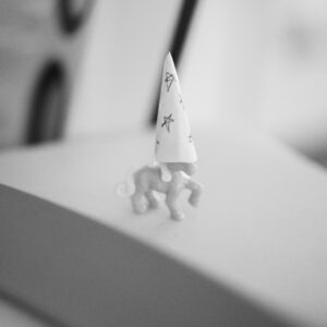 Ein Detailbild von einem Spielzeugpferd auf einem Schreibtisch. Es trägt einen selbstgebastelten Hut aus Papier mit kleinen, gemalten Sternen.